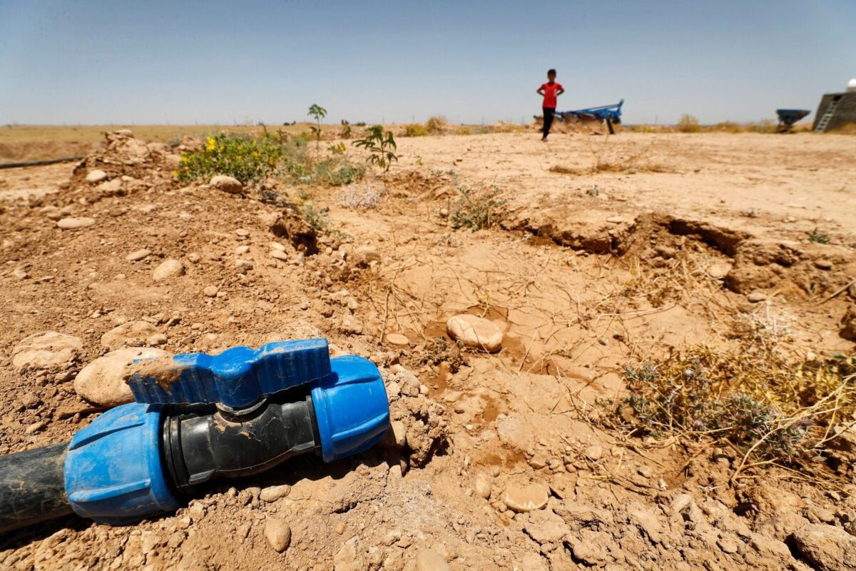 Menino caminha por um campo agrícola seco perto de uma mangueira sem água na área de Saadiya, ao norte de Diyala, no leste do Iraque, em junho 24 de 2021 [Ahmad Al-Rubaye / AFP via Getty Images]
