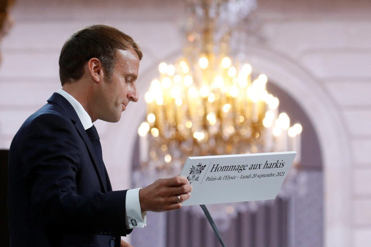Presidente da França Emmanuel Macron segura cartaz escrito “Homenagem aos harkis”, durante cerimônia em memória dos argelinos que serviram ao exército francês na Guerra de Independência, no Palácio do Eliseu, Paris, 20 de setembro de 2021 [GONZALO FUENTES/POOL/AFP via Getty Images]
