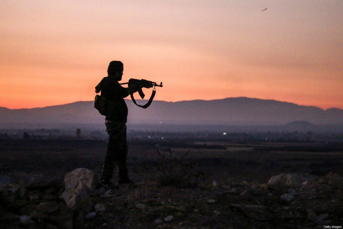 Um combatente rebelde sírio mira seu rifle Kalashnikov enquanto está perto da linha de frente contra as forças governamentais a oeste da cidade sulista de Daraa, em 3 de julho de 2018 [Mohamad Abazeed/AFP via Getty Images]
