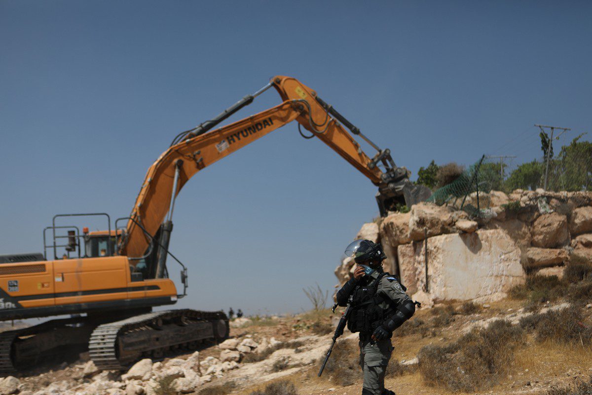Bulldozers israelenses apoiados por forças policiais derrubam uma oficina de manutenção de carros pertencente a uma família palestina na área de Harayik, Hebron, Cisjordânia, em 25 de agosto de 2021 [Mamoun Wazwaz/Agência Anadolu]