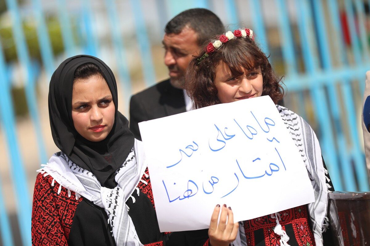 Os filhos da prisioneira palestina libertada Nisreen Abu Kamil seguram uma placa que diz 'Mamãe está a metros de nós' enquanto esperam que as autoridades da ocupação israelense a deixem entrar em Gaza, 18 de outubro de 2021 [Mustafa Hassona / Agência Anadolu]