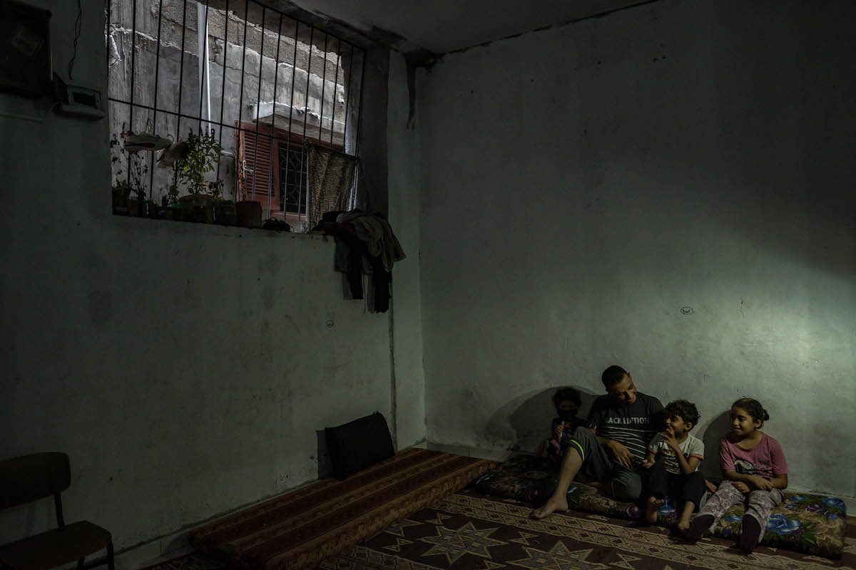 Mohammad al-Taramsi senta-se com seus filhos sob luzes de LED, devido aos apagões no campo de refugiados de Jabaliya, perto da Cidade de Gaza, em 29 de agosto de 2020 [Fatima Shbair/Getty Images]
