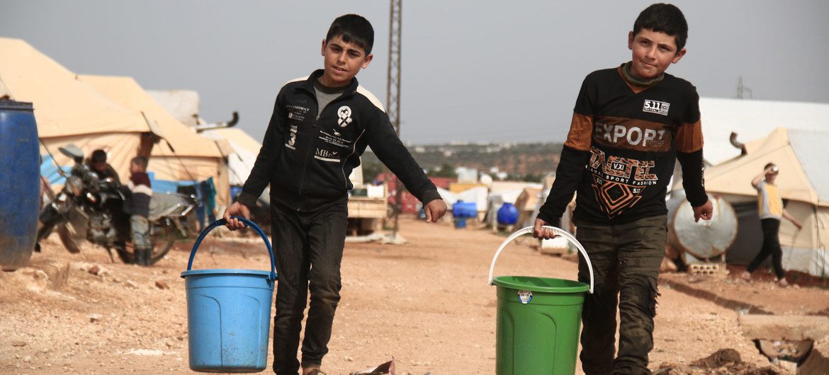 Crianças levam baldes com água em campo de deslocados na Síria [OCHA/Bilal al Hamoud]
