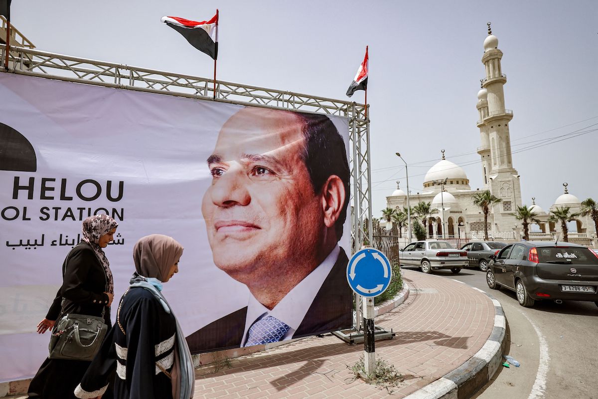 Mulheres passam por um enorme retrato de Abdel Fattah el-Sisi, às vésperas de uma visita da inteligência egípcia, na Cidade de Gaza, 31 de maio de 2021 [MOHAMMED ABED/AFP via Getty Images]
