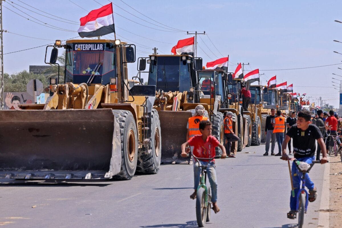 Meninos palestinos passam por um comboio de escavadeiras fornecidas pelo Egito que chegam ao lado palestino da passagem de fronteira de Rafah entre o Egito e o enclave palestino da Faixa de Gaza, em 4 de junho de 2021 [Said Khatib/AFP via Getty Images]