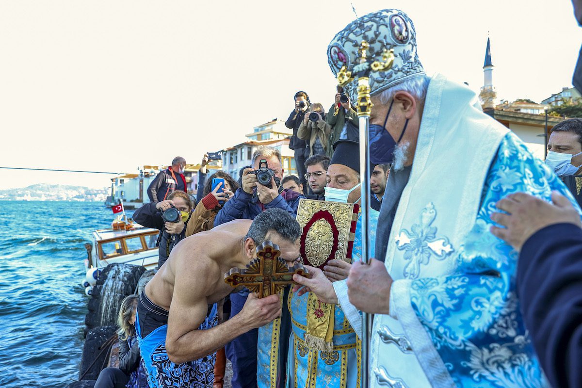 Um homem pega um crucifixo de madeira e o dá ao bispo metropolitano ortodoxo grego Kadikoy Emmanuel Adamakis (dir.) durante uma cerimônia de "lançamento de cruz" como parte das celebrações do batismo e nascimento de Jesus Cristo para abençoar a água no distrito de Uskudar, Turquia, em 06 de janeiro de 2022 [Serhat Çağdaş/Agência Anadolu]
