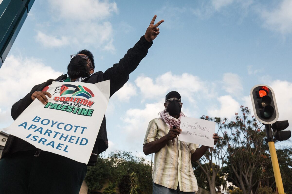 Apoiadores pró-palestinos seguram cartazes com os dizeres 'Boicote ao Apartheid Israel' durante um protesto para condenar os ataques aéreos israelenses em andamento em Gaza, em Durban, em 18 de maio de 2021 [Rajesh Jantilal/AFP via Getty Images]
