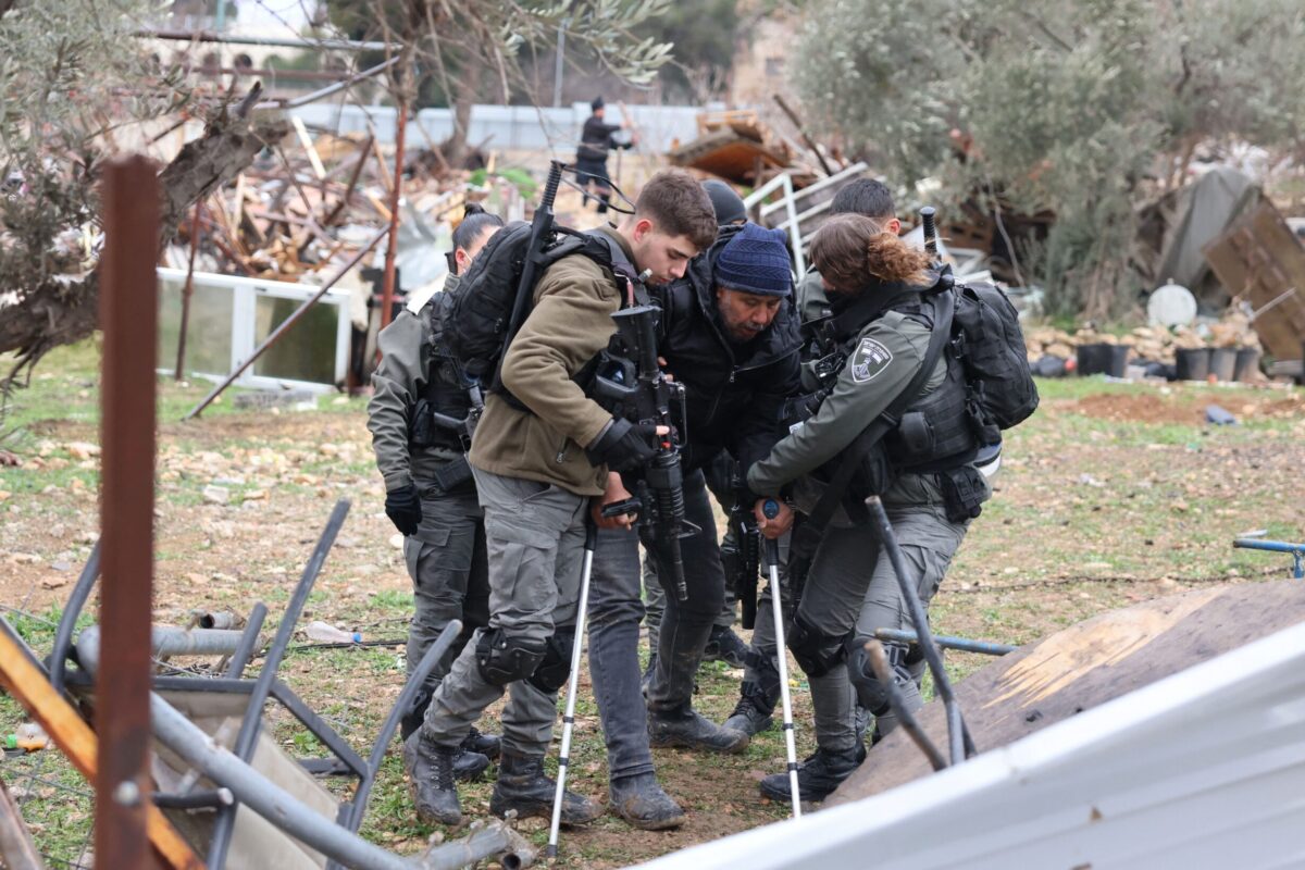 Forças israelenses escoltam um homem de muletas para longe das ruínas de uma casa palestina que demoliram, no bairro de Sheikh Jarrah, em 19 de janeiro de 2022 [Ahmad Gharabli/AFP via Getty Images]
