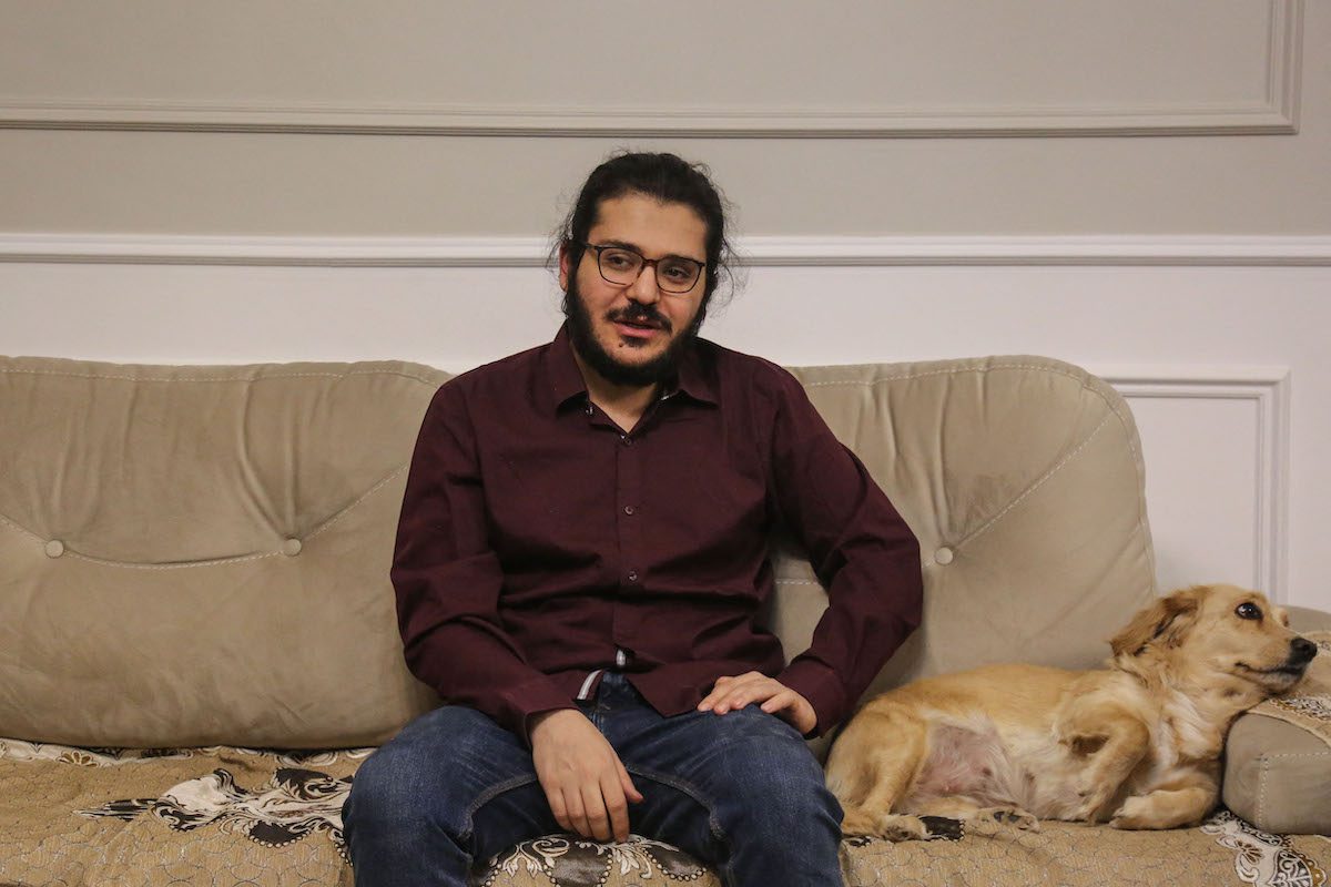 O pesquisador egípcio Patrick Zaki é fotografado ao lado de um cachorro na casa de sua família no Cairo, em 9 de dezembro de 2021, após sua libertação no início da semana [Mohamed El-Raai/AFP via Getty Images]
