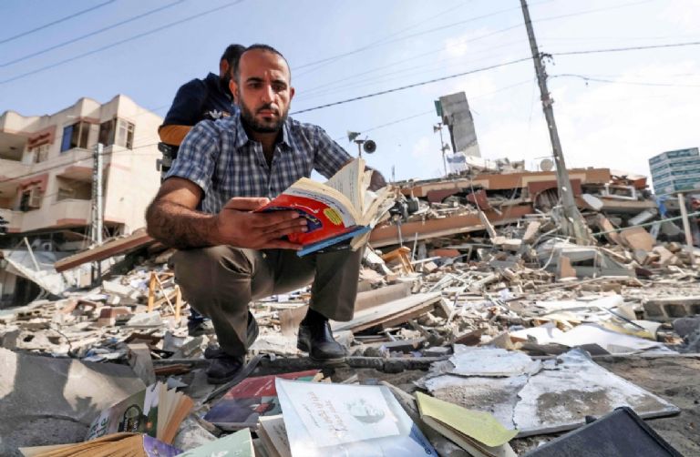 Homem folheia livro encontrado nos escombros da livraria de Samir Mansour, destruida por Israel em Gaza [Al-Quds/Twitter]
