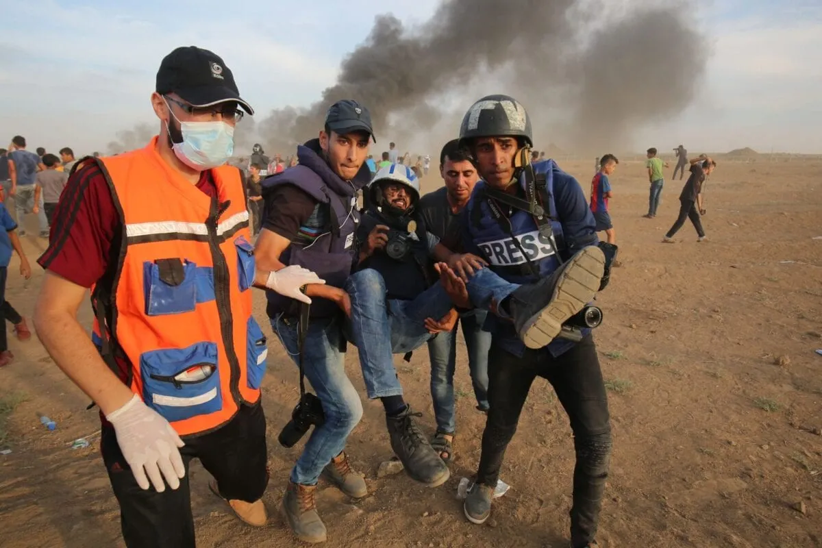 Paramédicos e jornalistas palestinos carregam um colega jornalista que foi ferido pelas forças israelenses, em 5 de outubro de 2018 [Said Khatib/AFP via Getty Images]

