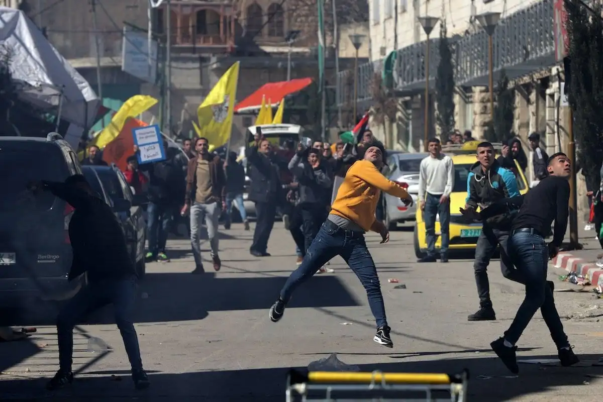 Manifestantes palestinos jogam pedras nos soldados israelenses em frente a um posto de controle em Hebron, Cisjordânia, em protesto contra os assentamentos ilegais de Israel. Em 28 de fevereiro de 2020. [Mamoun Wazwaz/Agência Anadolu]
