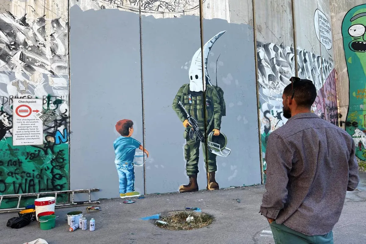 O artista palestino Taqi Spateen pinta as violações de soldados israelenses contra crianças palestinas em muro de discriminação em Belém, Cisjordânia, em 30 de maio de 2021 [Hisham K. K. Abu Shaqra/Agência Anadolu]
