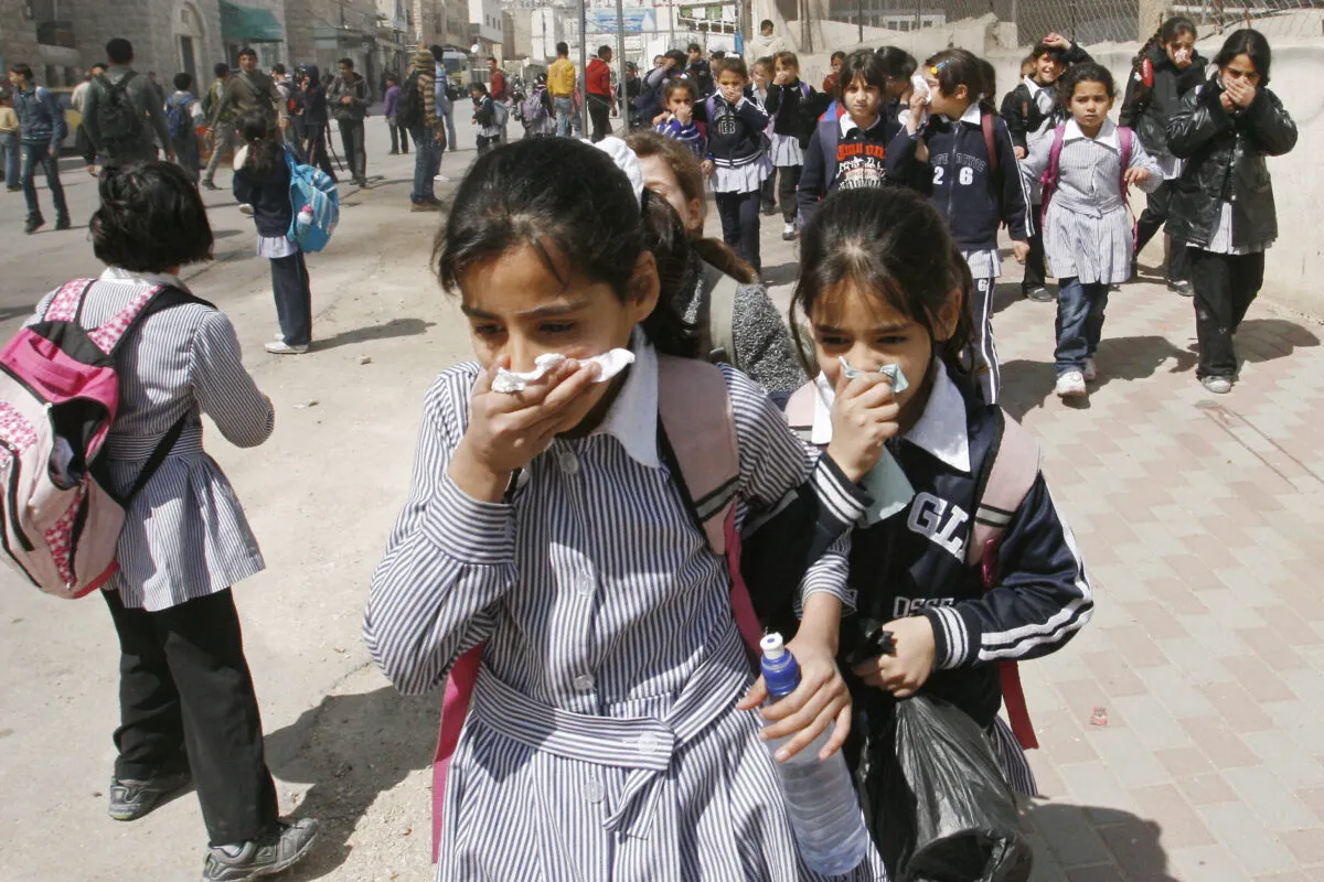 Estudantes palestinas cobrem seus rostos com gás lacrimogêneo em Hebron, na Cisjordânia ocupada, em 17 de março de 2010 [Hazem Bader/AFP via Getty Images]
