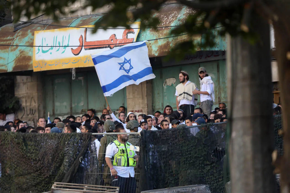 Colonos exibem bandeiras israelenses em Hebron (Al-Khalil), na Cisjordânia ocupada, em 19 de novembro de 2022 [Mamoun Wazwaz/Agência Anadolu]
