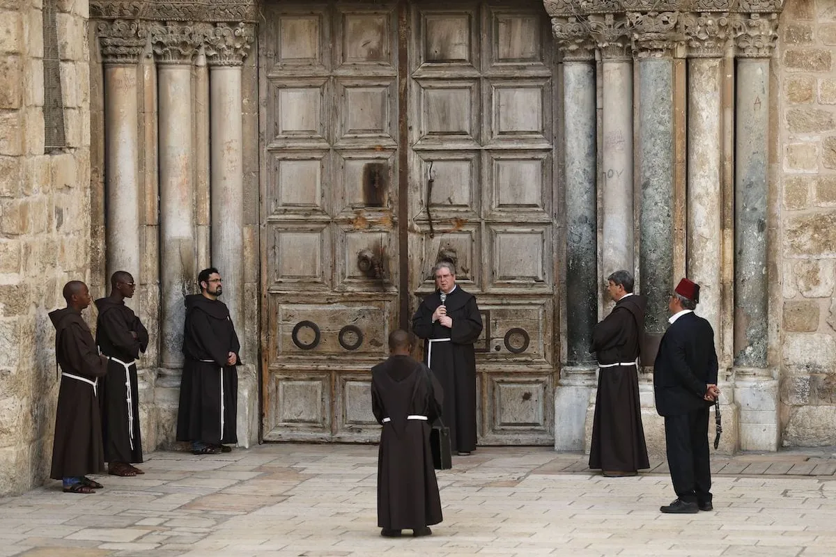 Monges franciscanos rezam em frente à porta fechada da Igreja do Santo Sepulcro, no bairro cristão da Cidade Velha de Jerusalém, em 27 de março de 2020, durante a crise do novo coronavírus [AHMAD GHARABLI/AFP via Getty Images]

