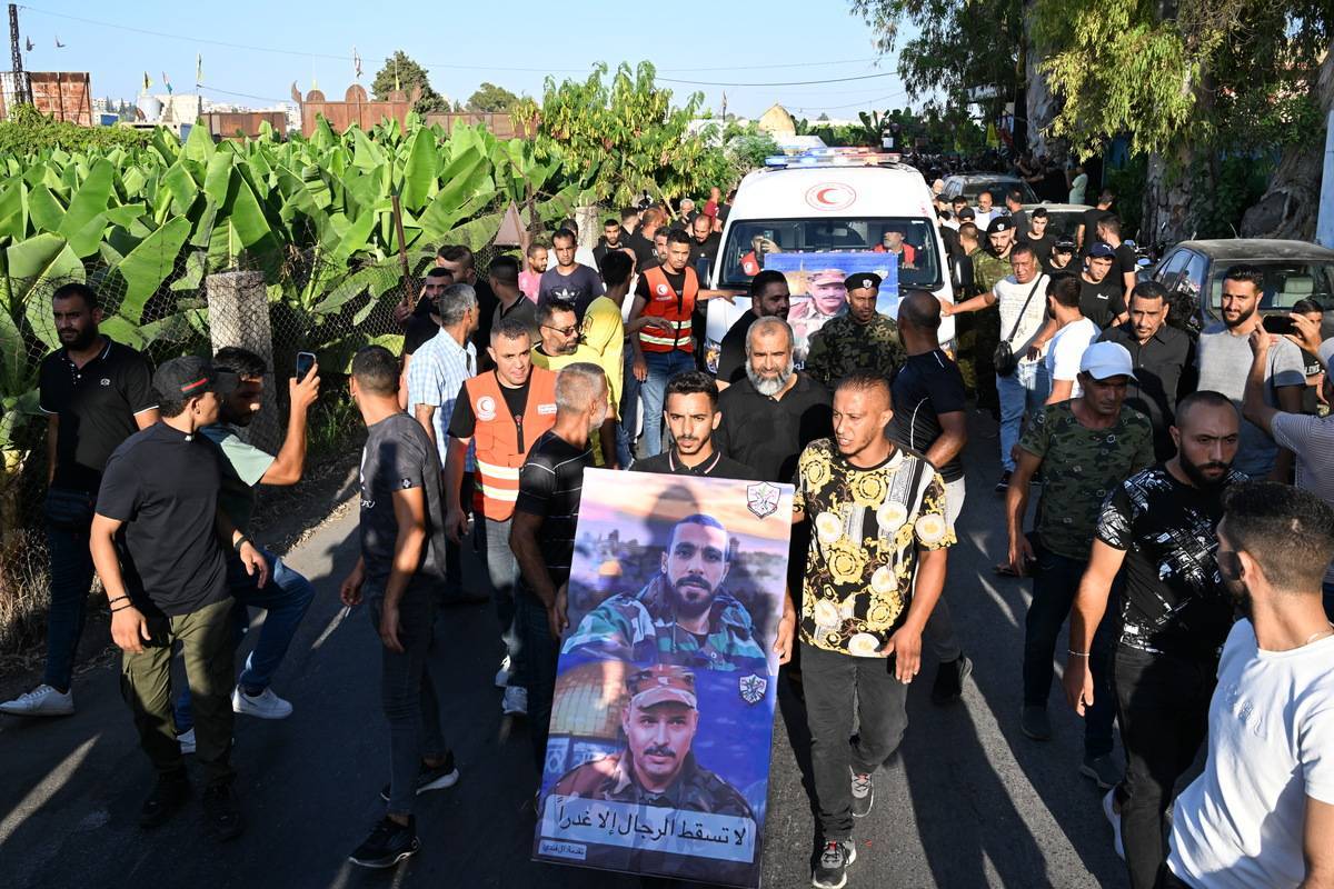 Um homem segura um cartaz entre as pessoas reunidas para a cerimônia fúnebre de Abu Sheref el-Armoushi, membro do Movimento Fatah e 3 guardas que foram mortos em confrontos entre duas frentes no campo de refugiados palestinos de Ain al-Helwa em Sidon, Líbano, em julho 31, 2023 [Houssam Shbaro/ Agência Anadolu]
