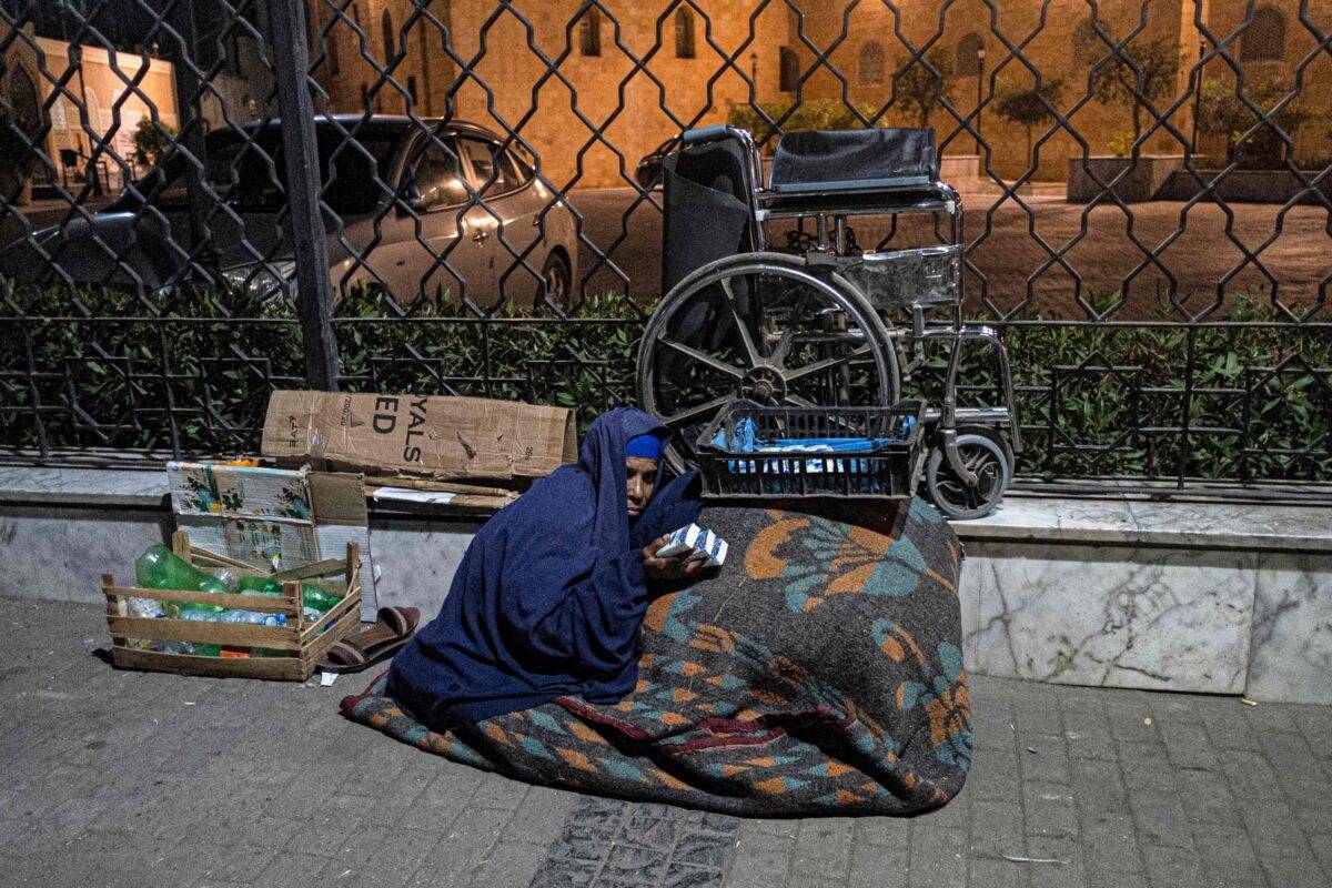Uma mendiga vende pacotes de lenços de papel ao longo da cerca da histórica mesquita Azhar no distrito de Azhar, capital do Egito, Cairo, em 16 de janeiro de 2023 [Khaled Desouki/AFP via Getty Images]
