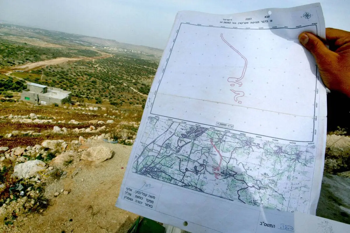 Um palestino mostra a ordem do exército israelense, assinada por Moshe Kaplinsky, o general encarregado da Cisjordânia, que mostra o caminho que as máquinas de terraplenagem israelenses seguirão ao cortar seu caminho pela Cisjordânia em 2 de dezembro de 2002 [David Silverman/Getty Images]
