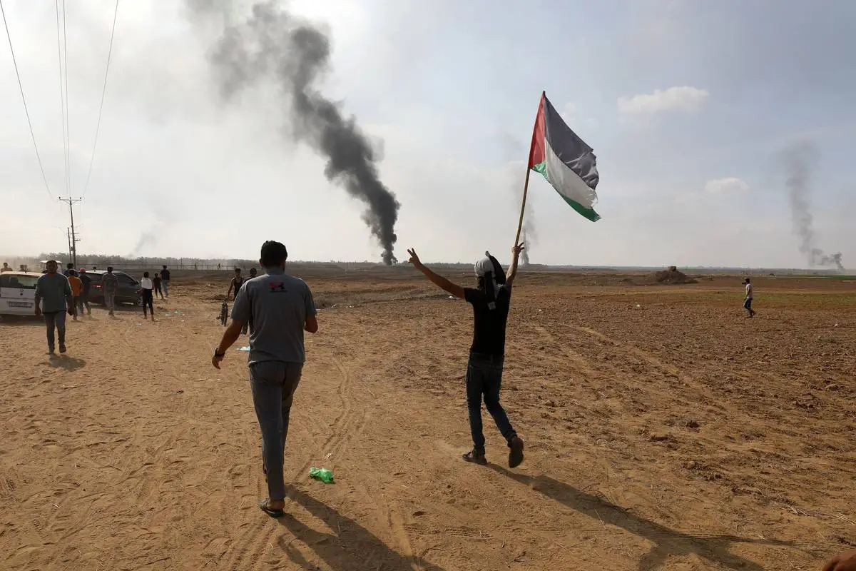Pessoas caminham com a bandeira palestina enquanto a fumaça sobe perto da fronteira entre Israel e Gaza na Faixa de Gaza, Gaza, em 7 de outubro de 2023. [Abed Rahim Khatib/Agência Anadolu].
