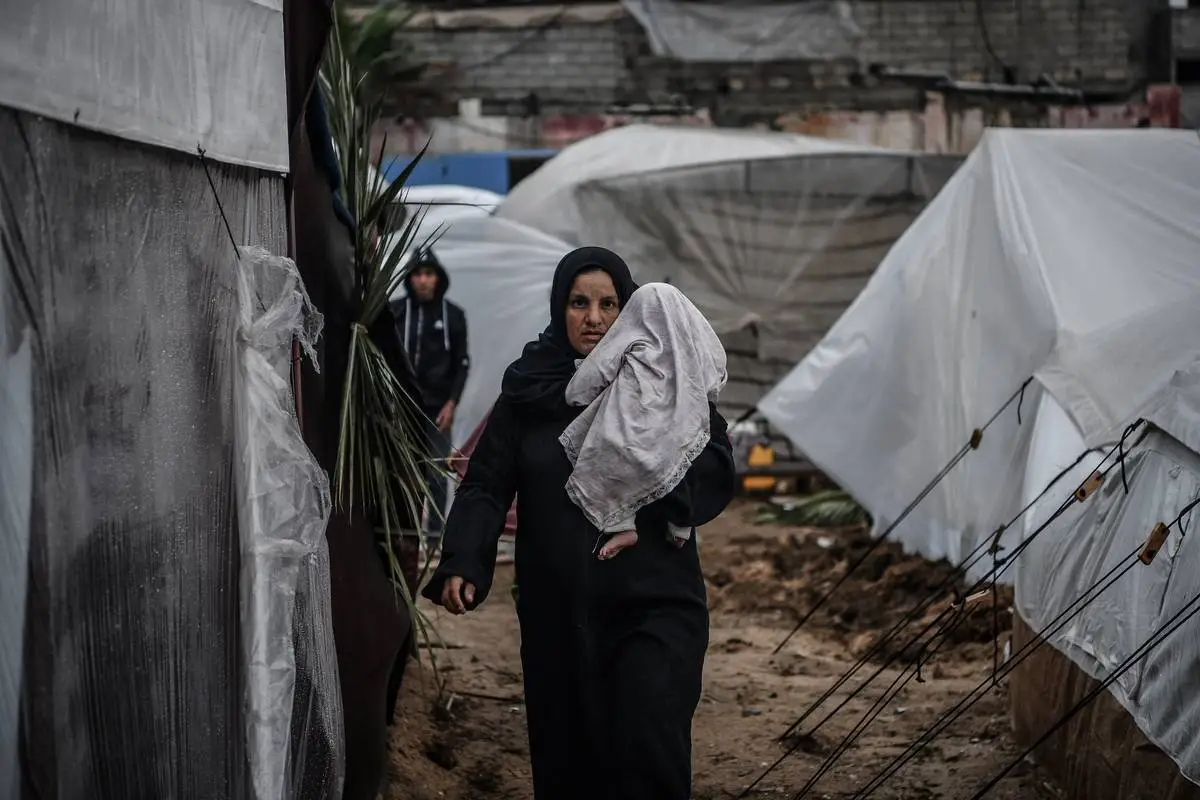 Mulher caminha com seu bebê entre as tendas improvisadas nos arredores do Hospital dos Mártires de Al-Aqsa, em meio aos bombardeios israelenses, em Khan Yunis, Gaza, em 19 de novembro de 2023 [Abed Zagout/Agência Anadolu]
