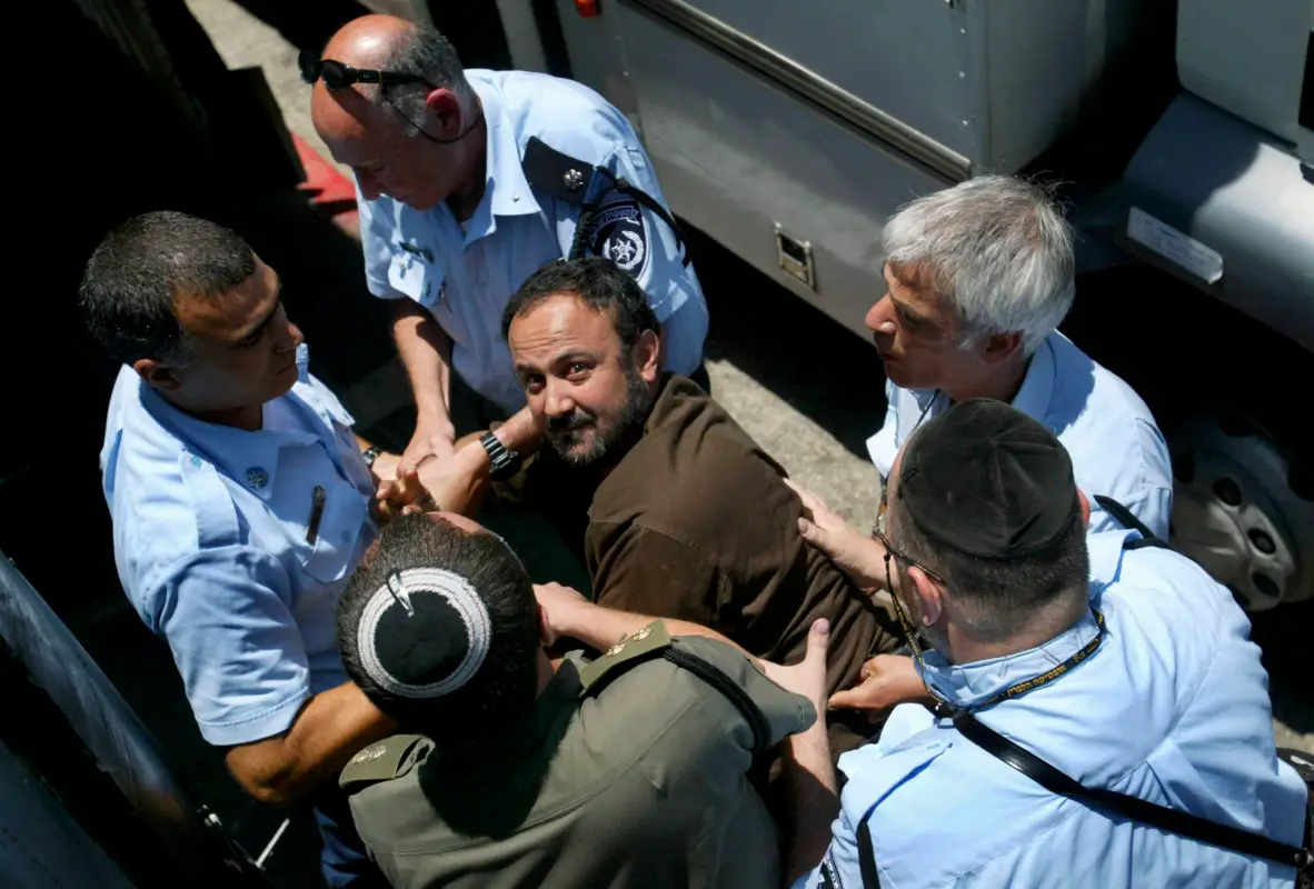 O líder palestino do Fatah na Cisjordânia, Marwan Barghuti, ladeado por guardas israelenses, chega a um tribunal de Tel Aviv em 6 de junho de 2004 em Israel [Uriel Sinai/Getty Images]
