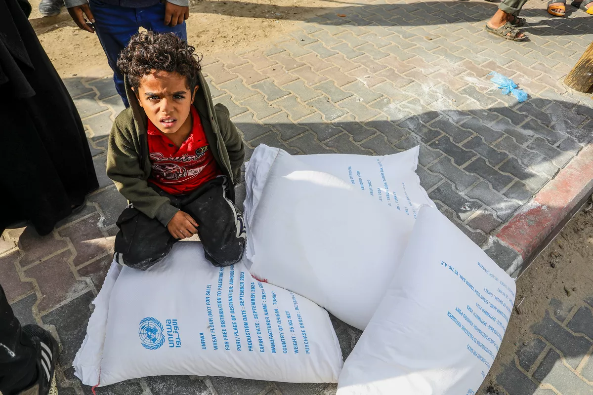 Criança recebe pacote de farinha da Agência das Nações Unidas para Assistência aos Refugiados da Palestina (UNRWA), em Rafah, no extremo sul de Gaza, em 21 de novembro de 2023 [Abed Rahim Khatib/Agência Anadolu]
