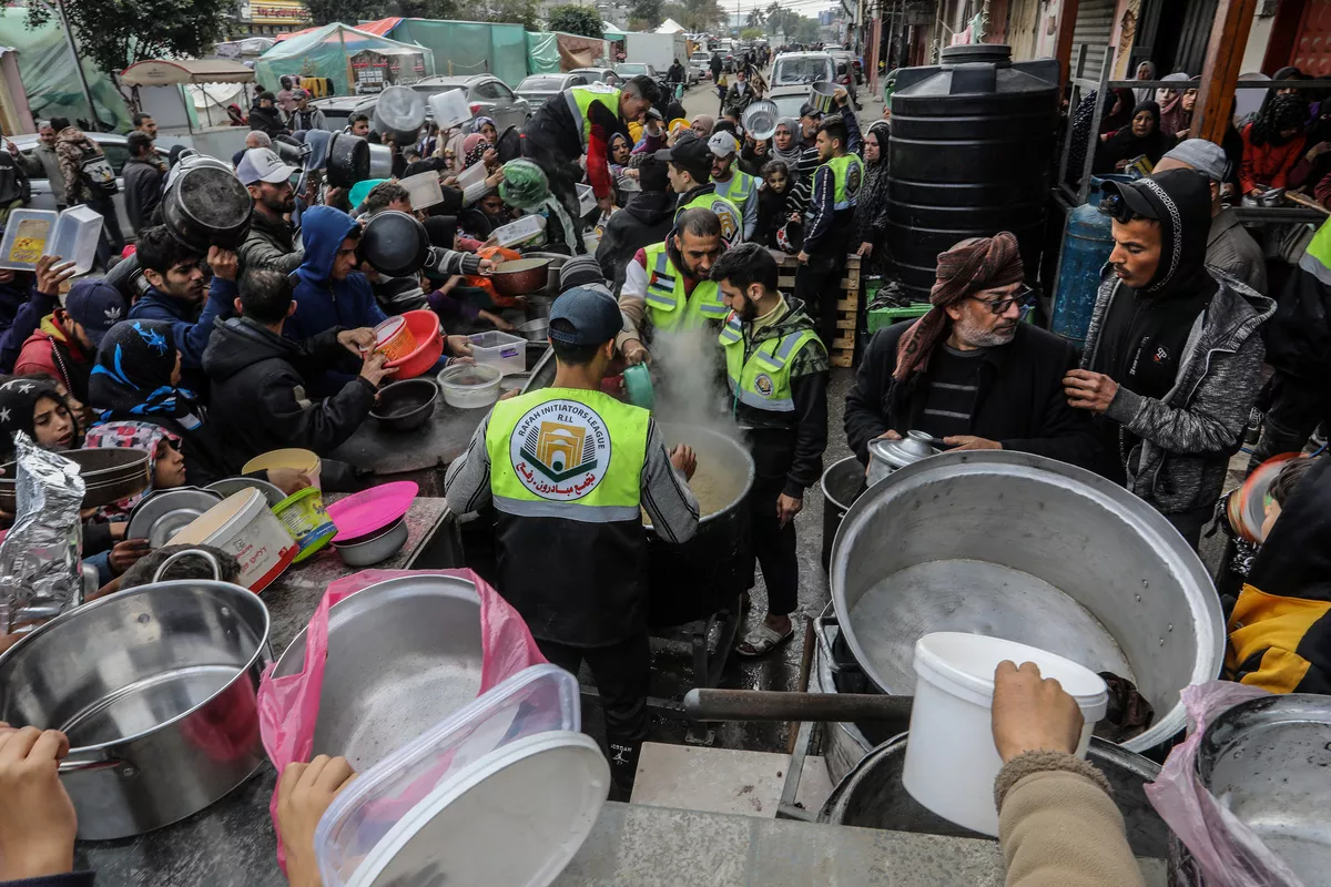 Palestinos segurando tigelas vazias tentam alcançar os alimentos distribuídos por voluntários no ponto de doação, enquanto os ataques israelenses continuam em Rafah, Gaza, em 26 de janeiro de 2024 [Abed Rahim Khatib/Anadolu Agency]
