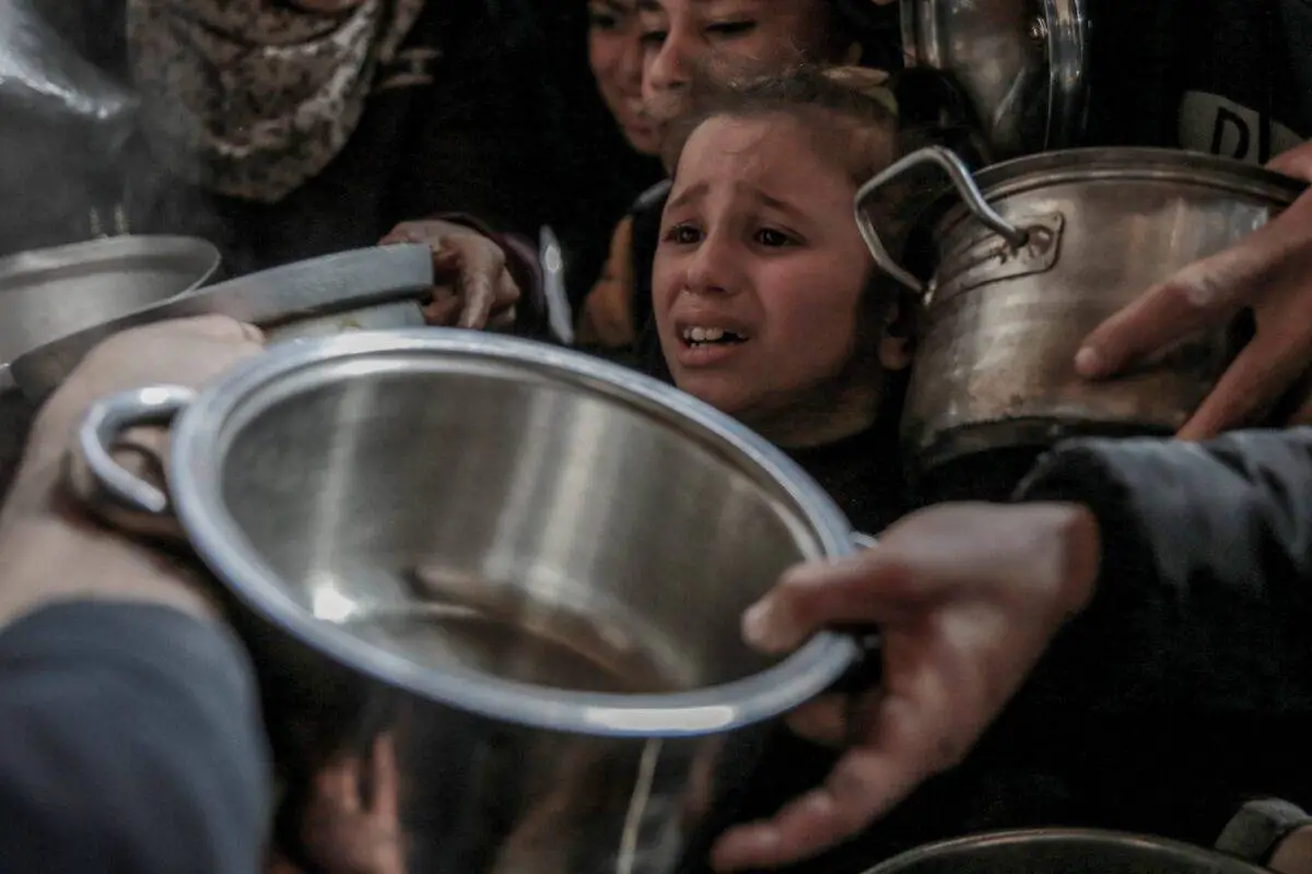 Uma criança é vista chorando em meio a outras com recipientes vazios, panelas, enquanto todas esperam para receber comida quente distribuída por organizações de caridade na Cidade de Gaza, Gaza, em 26 de fevereiro de 2024 [Omar Qattaa/Anadolu Agency]
