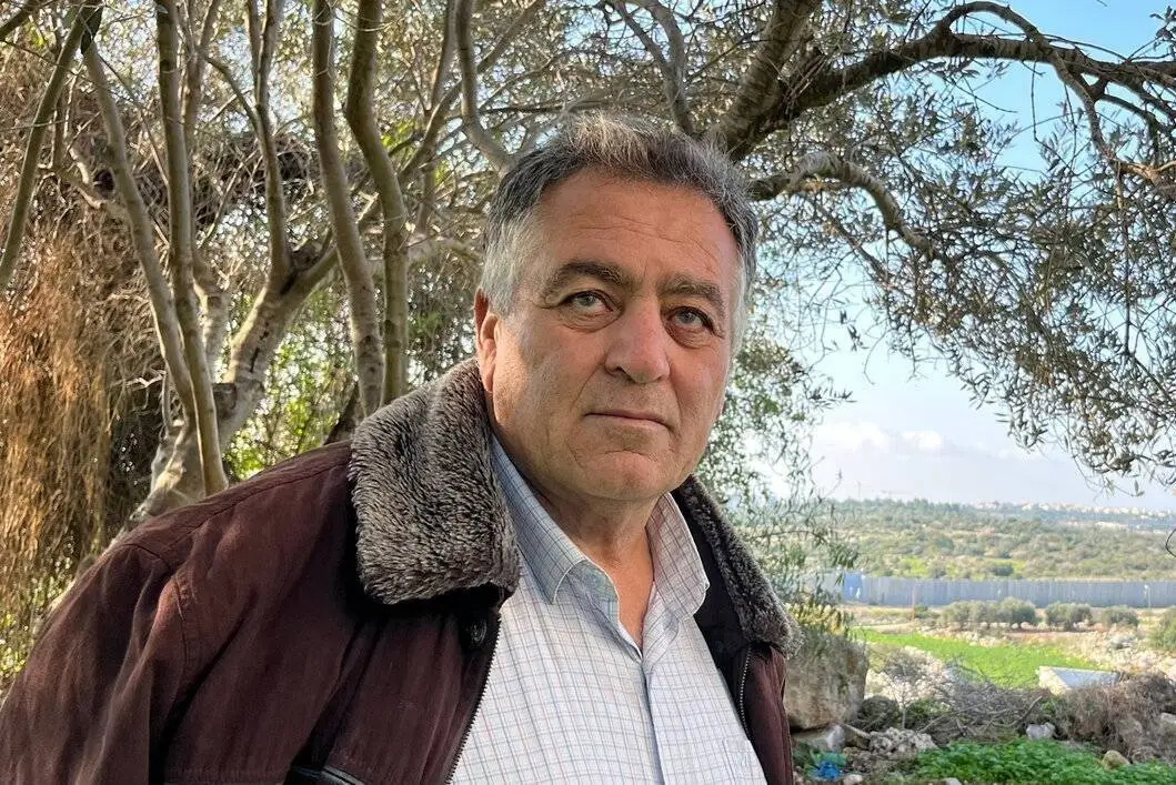 Tayseer Amarneh ao lado de uma árvore de oliveira no lado palestino do Muro do Apartheid, na Cisjordânia ocupada, em dezembro de 2023 [OCHA]
