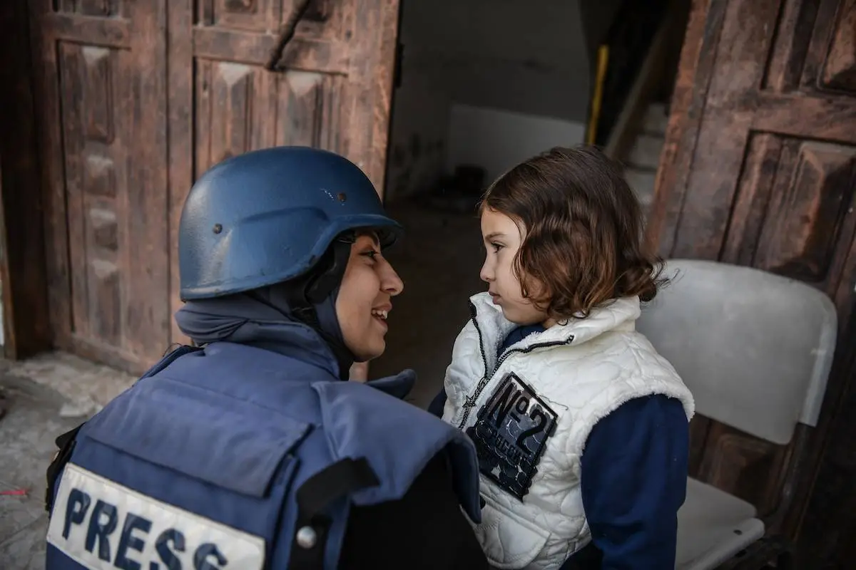 Reba Khalid al-Ajami, repórter da rede de notícias TRT Arabi, distrai sua filha em meio aos bombardeios de Israel a Rafah, no extremo sul de Gaza, em 29 de fevereiro de 2024 [Abed Zagout/Agência Anadolu]
