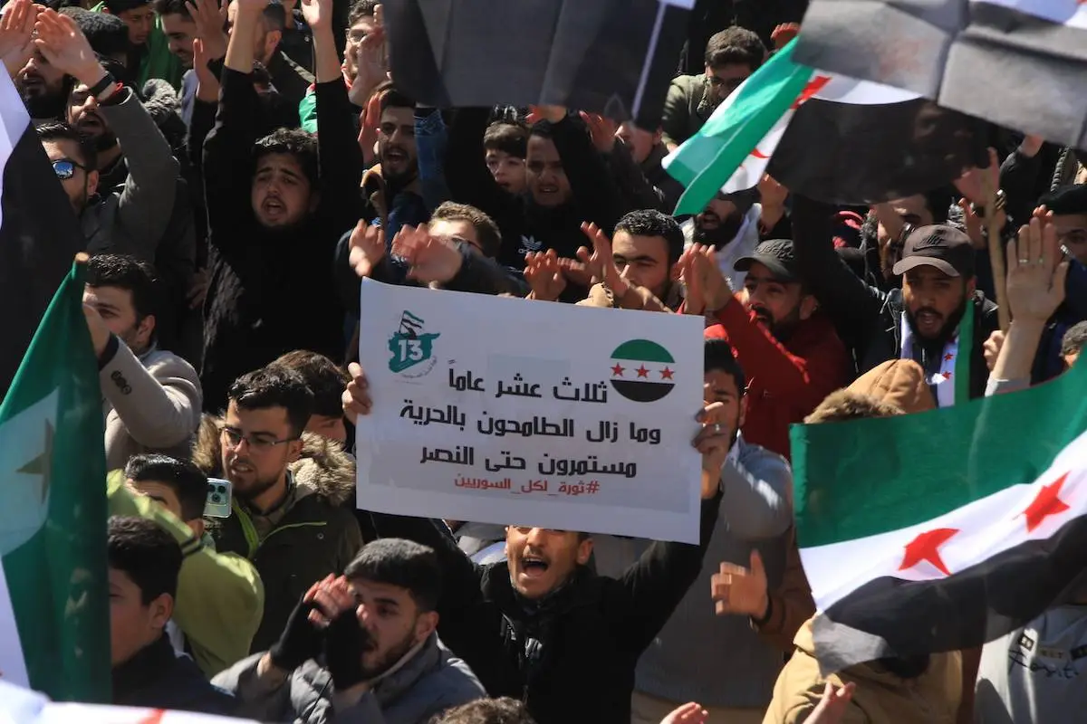 Sírios, segurando bandeiras e proferindo slogans, fazem uma manifestação contra o regime de Bashar al-Assad no 13º aniversário da Guerra Civil Síria no distrito de Azaz, em Aleppo, Síria, em 15 de março de 2024 [Hişam Hac Ömer/Agência Anadolu]