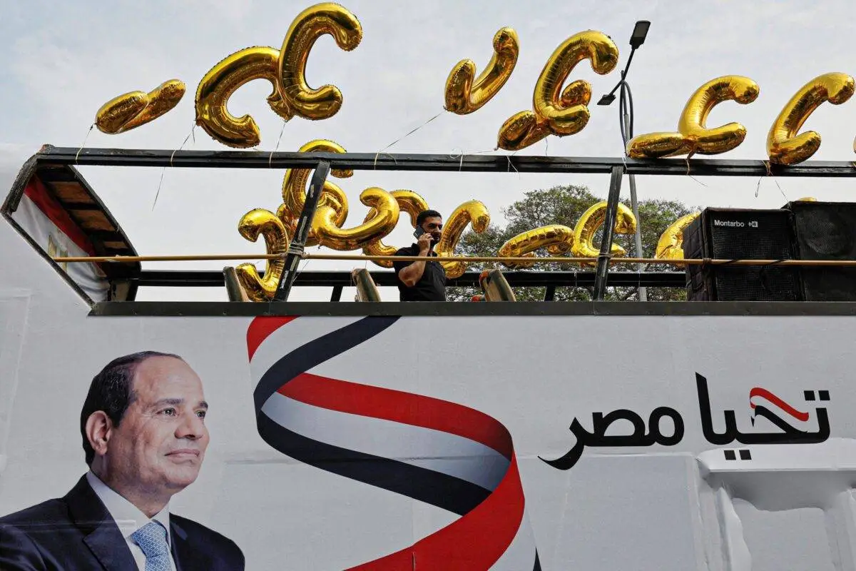 Um homem fala ao telefone em cima de um ônibus de campanha eleitoral do presidente do Egito, Abdel Fattah al-Sisi, adornado com sua imagem, seu slogan "viva o Egito" e balões em forma de C em Gizé, em 2 de outubro de 2023 [Khaled Desouki/AFP via Getty Images]