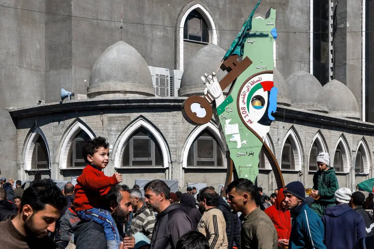 Foto: Pessoas passam por um cartaz que representa um mapa da Palestina histórica, mostrando uma mão que se estende para fora da Faixa de Gaza segurando uma chave, com uma legenda em árabe que diz "distância para Jerusalém 108 km", exibido do lado de fora de uma mesquita em Rafah, no sul da Faixa de Gaza, em 08 de fevereiro de 2024 [Mohammed Abed/AFP via Getty Images]
