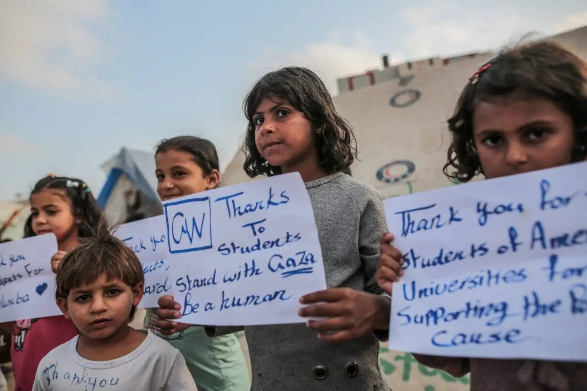 Crianças palestinas, deslocadas devido aos ataques israelenses e vivendo em barracas na cidade de Rafah, em Gaza, organizam uma manifestação para expressar gratidão aos estudantes das universidades que protestam contra os ataques israelenses em 1º de maio de 2024 [Jehad Alshrafi/Agência Anadolu]
