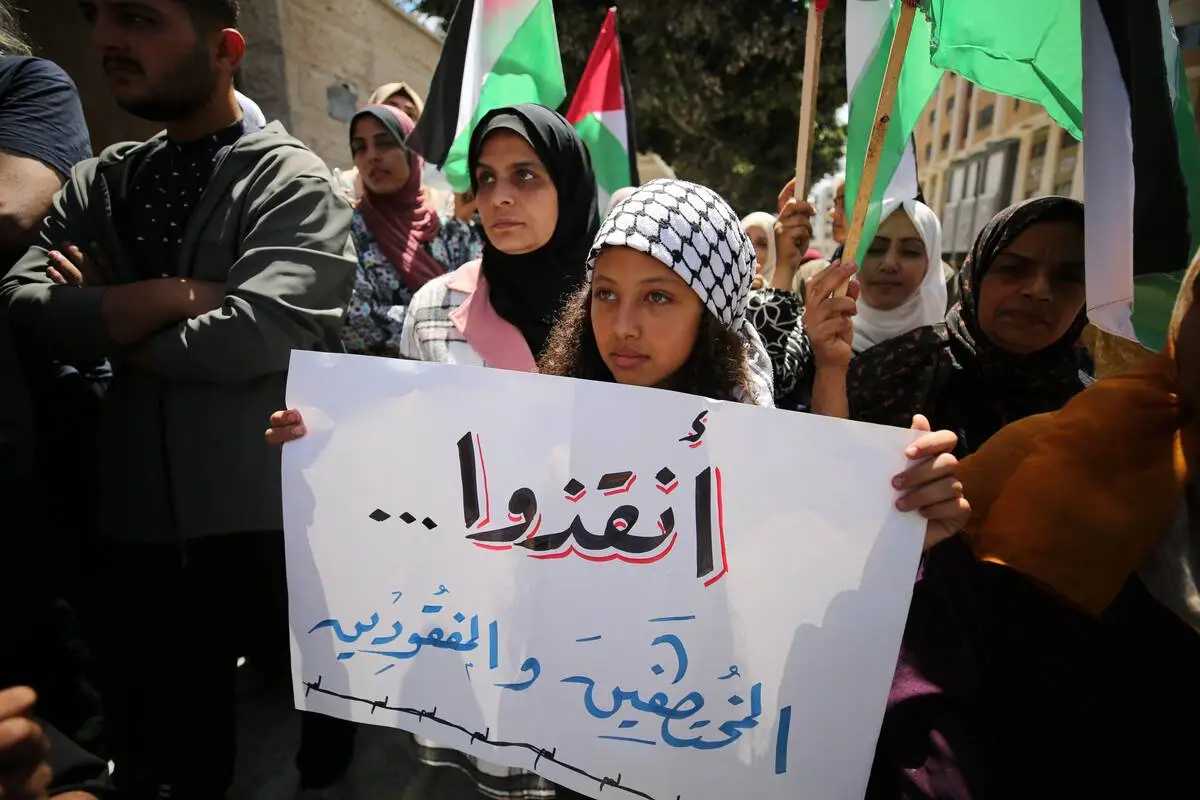 Manifestantes palestinos seguram faixas e cartazes em frente ao prédio do Movimento Internacional da Cruz Vermelha e do Crescente Vermelho (CICV) durante um protesto realizado para apoiar os palestinos presos nas prisões israelenses, na Cidade de Gaza, Gaza, em 06 de maio de 2024. [Dawoud Abo Alkas - Agência Anadolu]