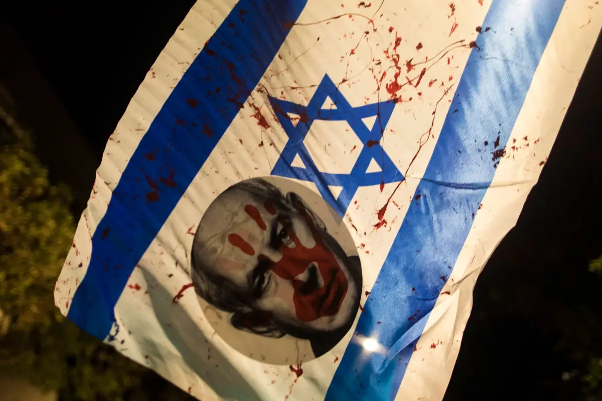 Uma bandeira israelense coberta de sangue e um adesivo do primeiro-ministro israelense, Benjamin Netanyahu, vistos durante um protesto pedindo a renúncia de Netanyahu em 4 de novembro de 2023 em Jerusalém [Amir Levy/Getty Images]
