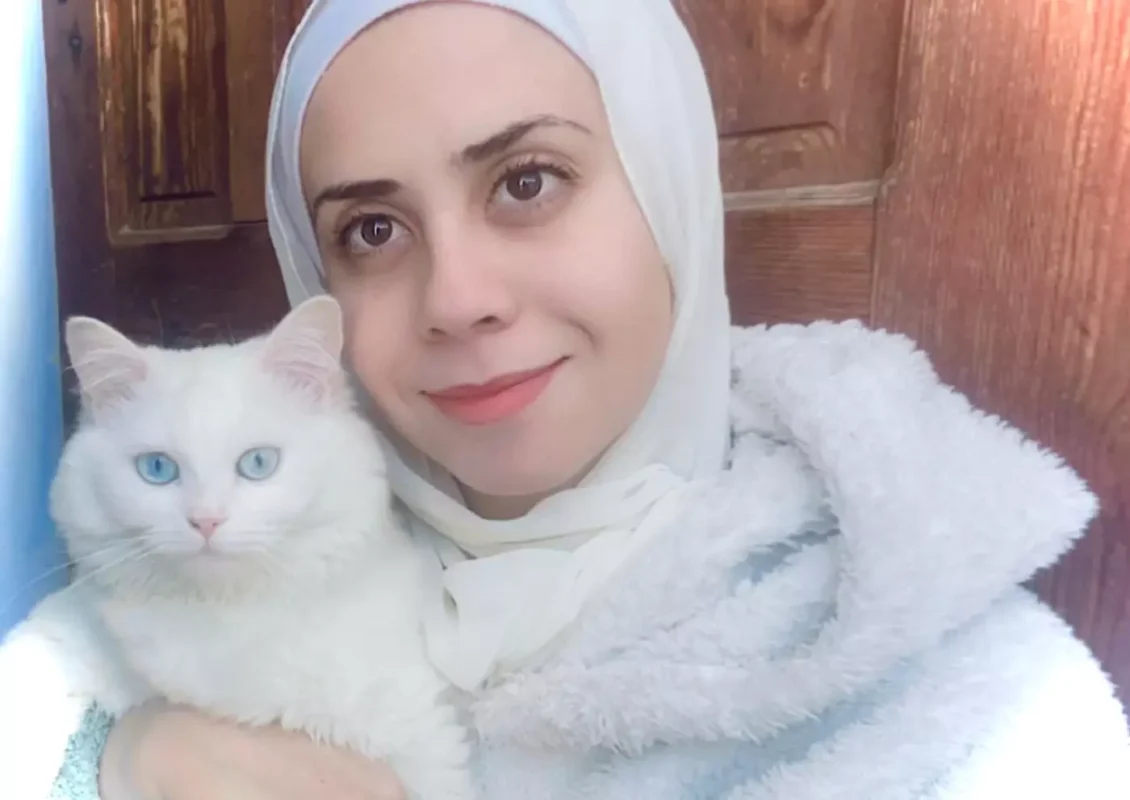 A autora posa para uma selfie com seu gato Beasty enquanto procuram abrigo na casa de um parente em abril de 2024 [Tarneem Hammad/ Arquivo pessoal]
