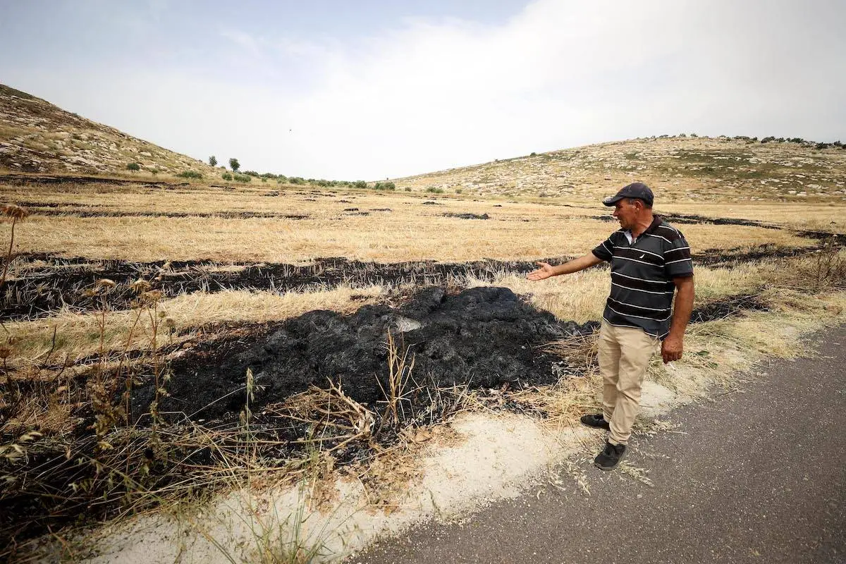 Palestino mostra uma terra queimada depois que um grupo de colonos judeus queimou veículos pertencentes a palestinos, na Cisjordânia, em 26 de maio de 2023 [Issam Rimawi/Agência Anadolu]
