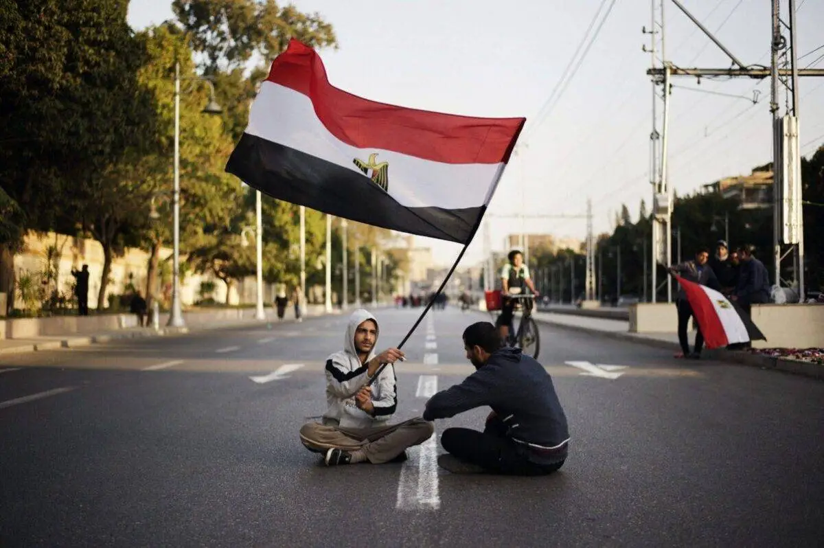 Manifestantes egípcios antigoverno sentam-se agitando sua bandeira nacional do lado de fora do palácio presidencial egípcio no Cairo durante uma manifestação em 8 de fevereiro de 2013 [Gianluigi Guercia/AFP via Getty Images]
