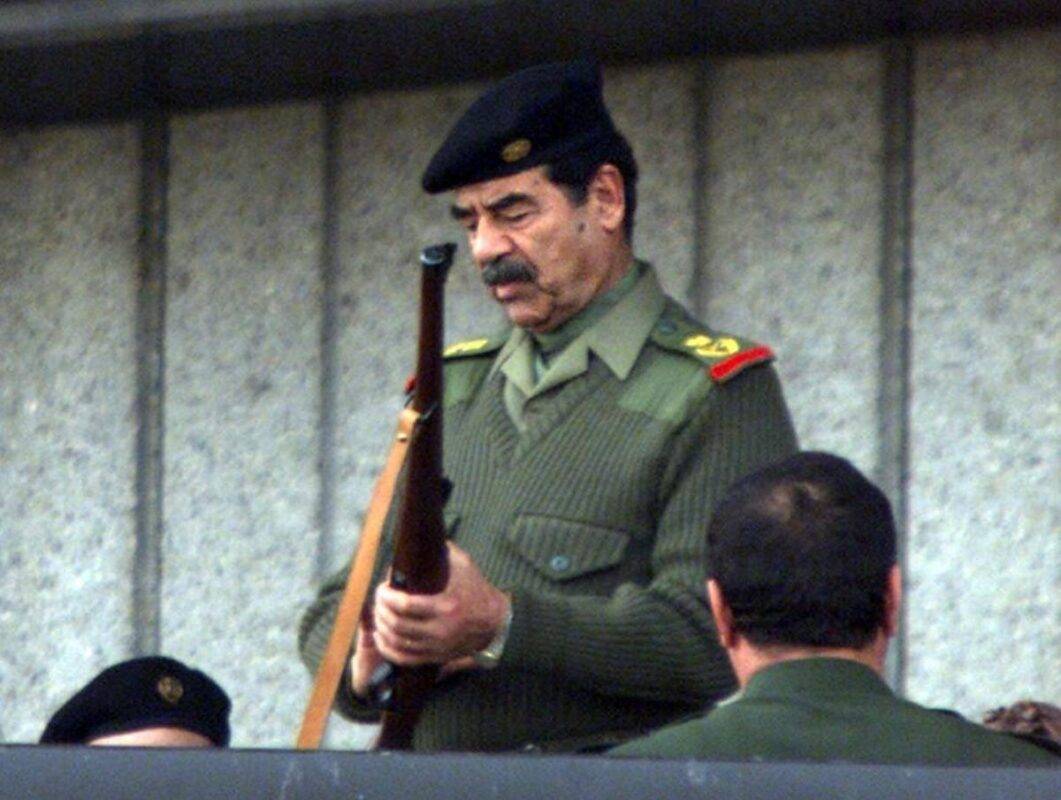 Então presidente do Iraque, Saddam Hussein, prepara sua arma para dar o sinal ao início de um desfile militar em Bagdá, em 20 de novembro de 2000 [Karim Sahib/AFP via Getty Images]
