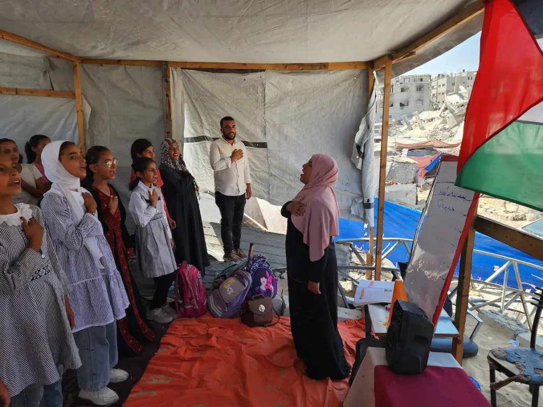 Os alunos cantam o hino nacional na escola de tendas, na qual seu professor Alaa Abu Mustafa, cuja casa foi destruída nos ataques do exército israelense, dá-lhes educação em Khan Yunis, Gaza, em 3 de setembro de 2024. [Hani Alshaer - Agência Anadolu].
