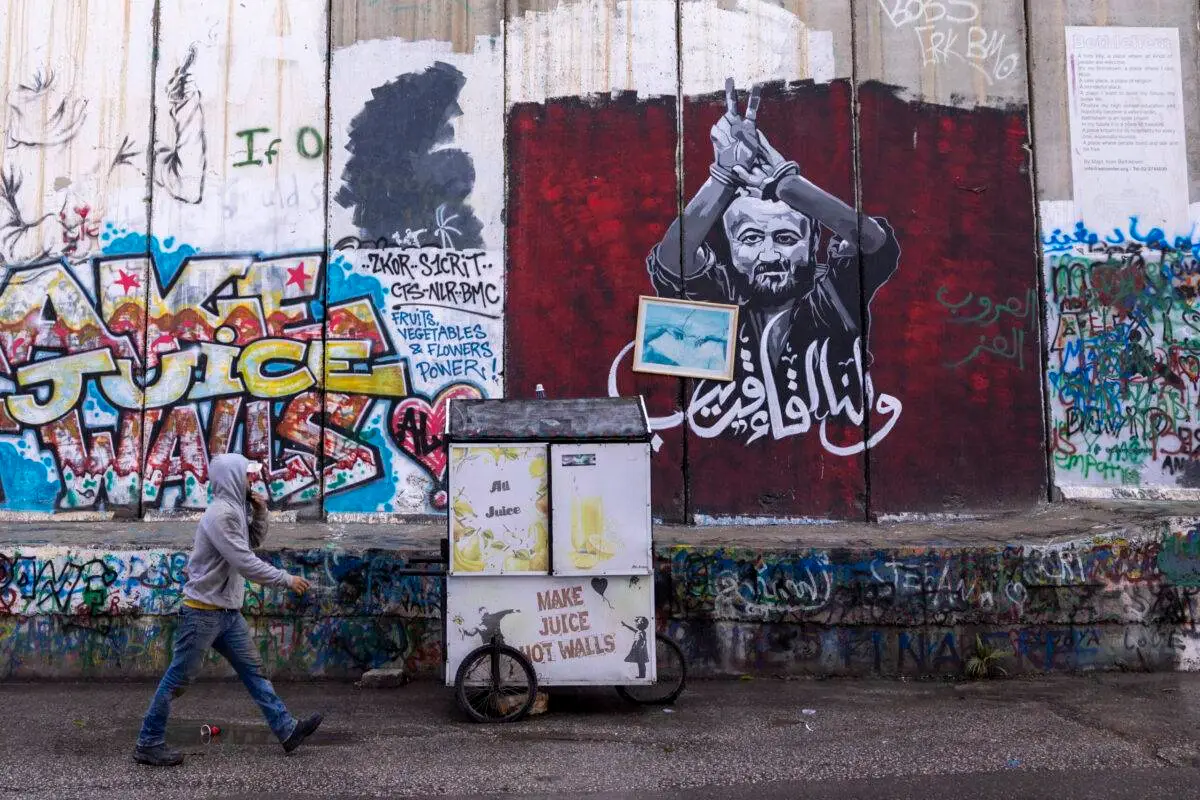 Um homem palestino passa pelo grafite mostrando Marwan Barghouti, um político palestino preso em 24 de dezembro de 2023 em Belém, Cisjordânia [Maja Hitij/Getty Images]
