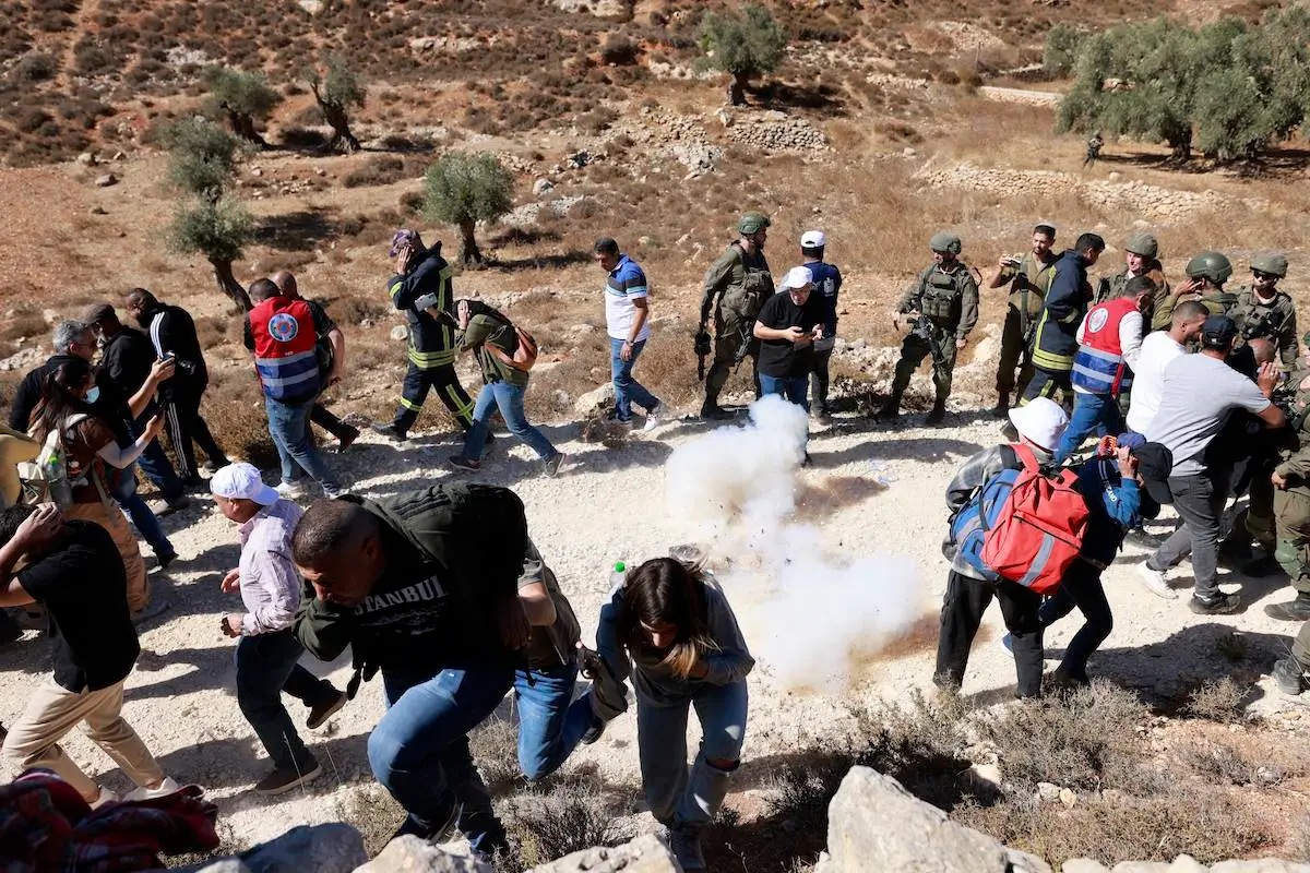 Soldados israelenses lançam uma granada sonora para dispersar fazendeiros palestinos, impedindo-os de colher azeitonas em seus campos, na vila de Burqa, a leste de Ramallah, na Cisjordânia ocupada por Israel, em 20 de outubro de 2024. [Jaafar Ashttiyeh/AFP via Getty Images]