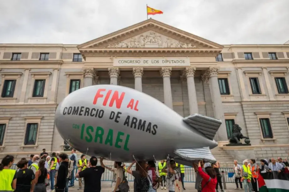 Pessoas carregando uma bomba inflável com os dizeres "Acabem com o comércio de armas com Israel" passam pelo Parlamento Espanhol em Madri, Espanha, em 5 de outubro de 2024 [Marcos del Mazo/LightRocket via Getty Images]