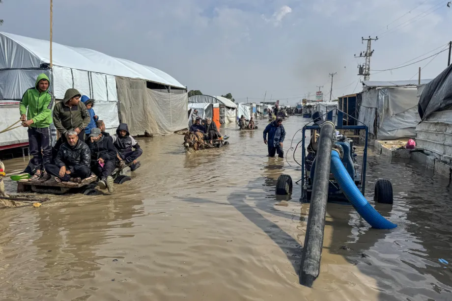 Palestinos tentam atravessar uma rua alagada usando carroças puxadas por cavalos, burros e mulas, além de motocicletas, após fortes chuvas na área de Al-Mawasi, em Khan Yunis, Gaza, em 24 de fevereiro de 2026. [Abdallah F.s. Alattar – Agência Anadolu]