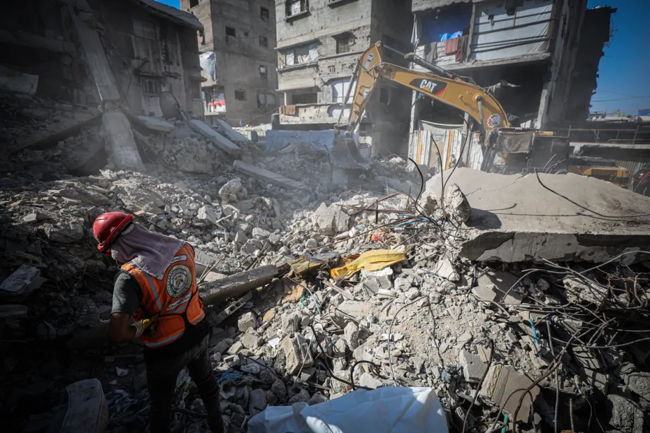 Um membro da Defesa Civil Palestina trabalha entre os escombros enquanto uma escavadeira remove os destroços de uma casa destruída pertencente à família Sawafiri, durante operações de busca e resgate realizadas em coordenação conjunta com o Comitê Internacional da Cruz Vermelha (CICV), na Cidade de Gaza, Gaza, em 18 de agosto de 2026. [Hamza Z. H. Qraiqea – Anadolu Agency]