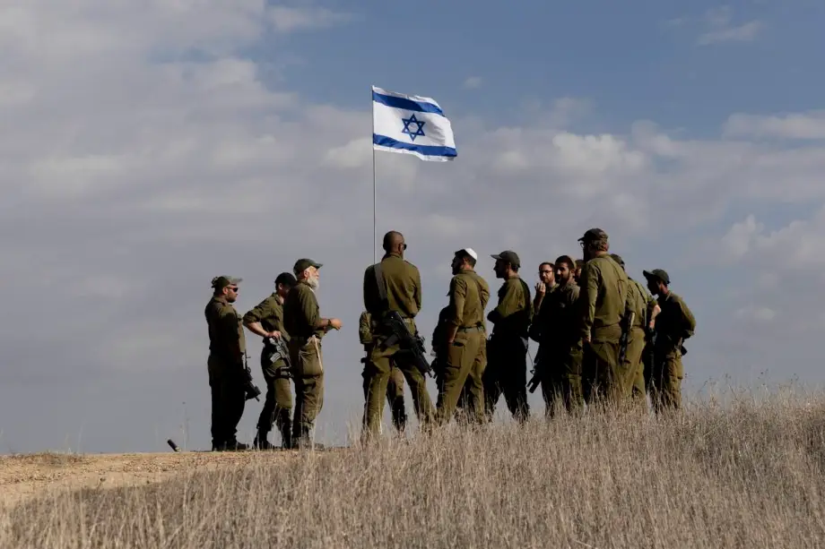 Soldados permanecem próximos a uma bandeira israelense enquanto recebem instruções perto da fronteira com a Faixa de Gaza, em 5 de dezembro de 2024, no sul de Israel. [Amir Levy/Getty Images]