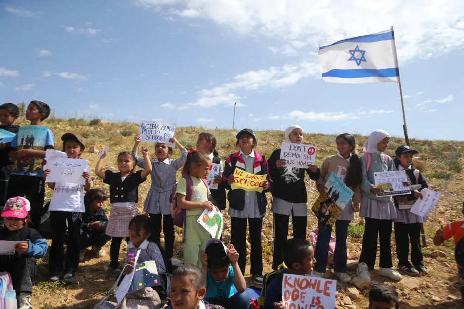 Estudantes palestinos, segurando faixas, e ativistas que apoiam estudantes que estão impedidos de frequentar a escola há quase duas semanas e privados de seu direito à educação devido ao bloqueio da estrada por israelenses, organizam uma manifestação na área onde a estrada foi fechada para protestar contra o fechamento do acesso à escola na aldeia de Umm al-Khair, na região de Masafer Yatta, ao sul de Hebron, na Cisjordânia, Palestina, em 26 de abril de 2026. [Wisam Hashlamoun – Agência Anadolu]

