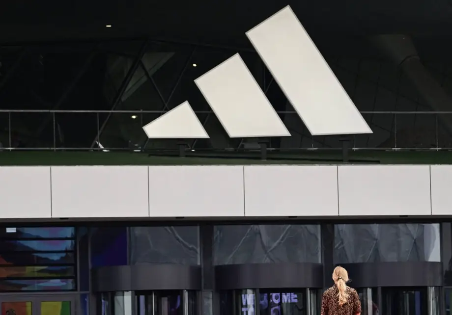 Uma mulher passa sob um enorme logotipo na sede da Adidas, fabricante alemã de artigos esportivos, em Herzogenaurach, no sul da Alemanha, em 21 de junho de 2024. [Tobias Schwarz via Getty Images]